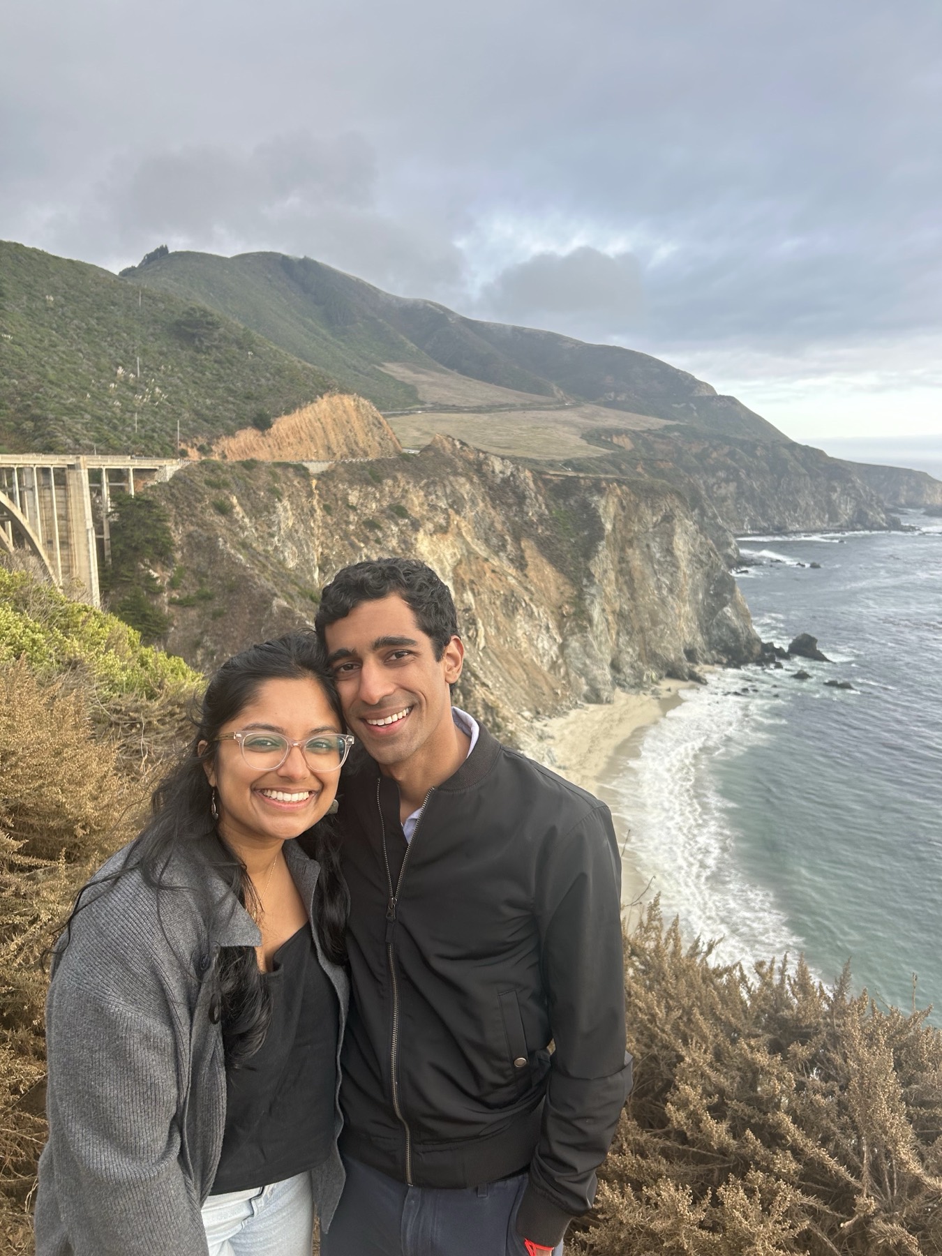 Manu and Nikhil above the coast at Big Sur, with Bixby Bridge behind them